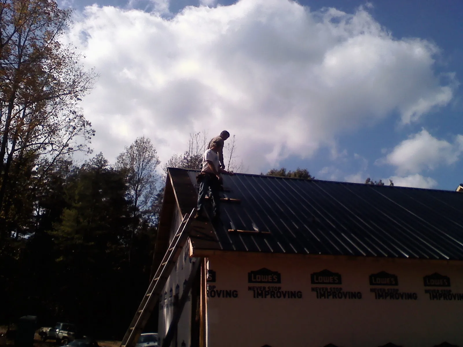 Roofer fastening dark metal panels high against a cloudy sky, from a Roof Inspection job in Cleveland